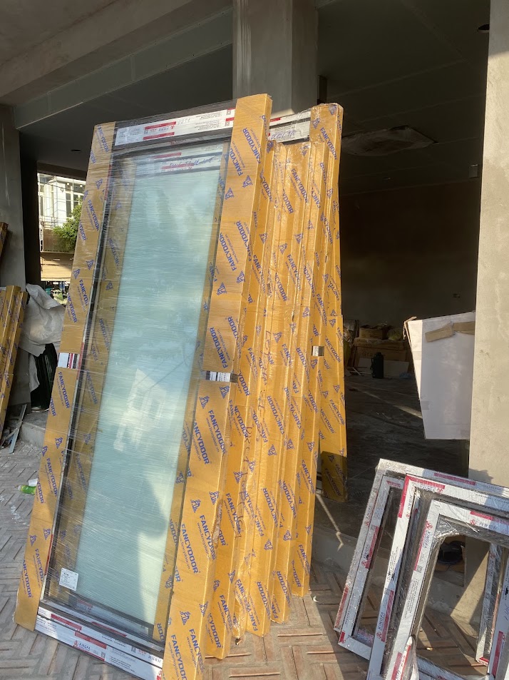 Cửa kính nhôm Xingfa FamiDoor mới, còn bọc bảo vệ, xếp trước công trình đang thi công